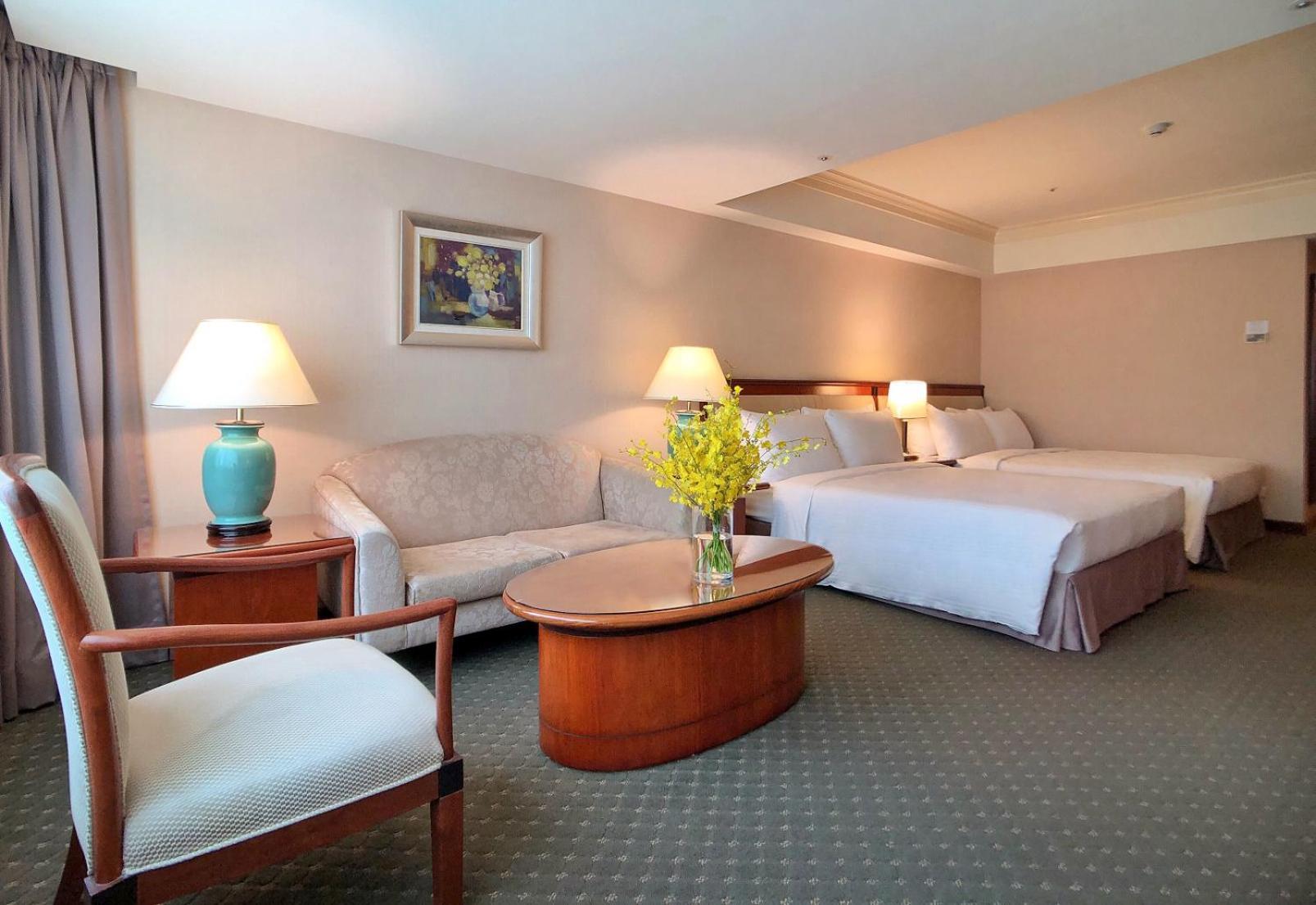 Evergreen Laurel Hotel - Taizhong Zewnętrze zdjęcie The photo shows a hotel room featuring two beds, a small seating area, and a coffee table. The walls are painted in soft, neutral colors, and there is a framed piece of artwork hanging on the wall. A potted plant with yellow flowers is placed on the 