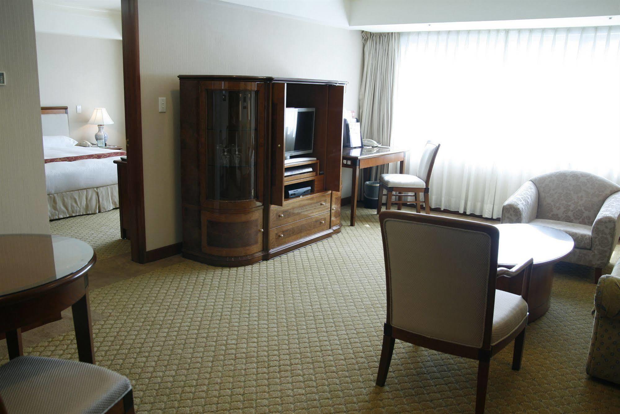 Evergreen Laurel Hotel - Taizhong Zewnętrze zdjęcie The photo shows an interior of a hotel room suite. The space includes a living area with several pieces of furniture. There is a coffee table and chairs, creating a comfortable seating area. A wooden cabinet with a TV inside is situated against one w