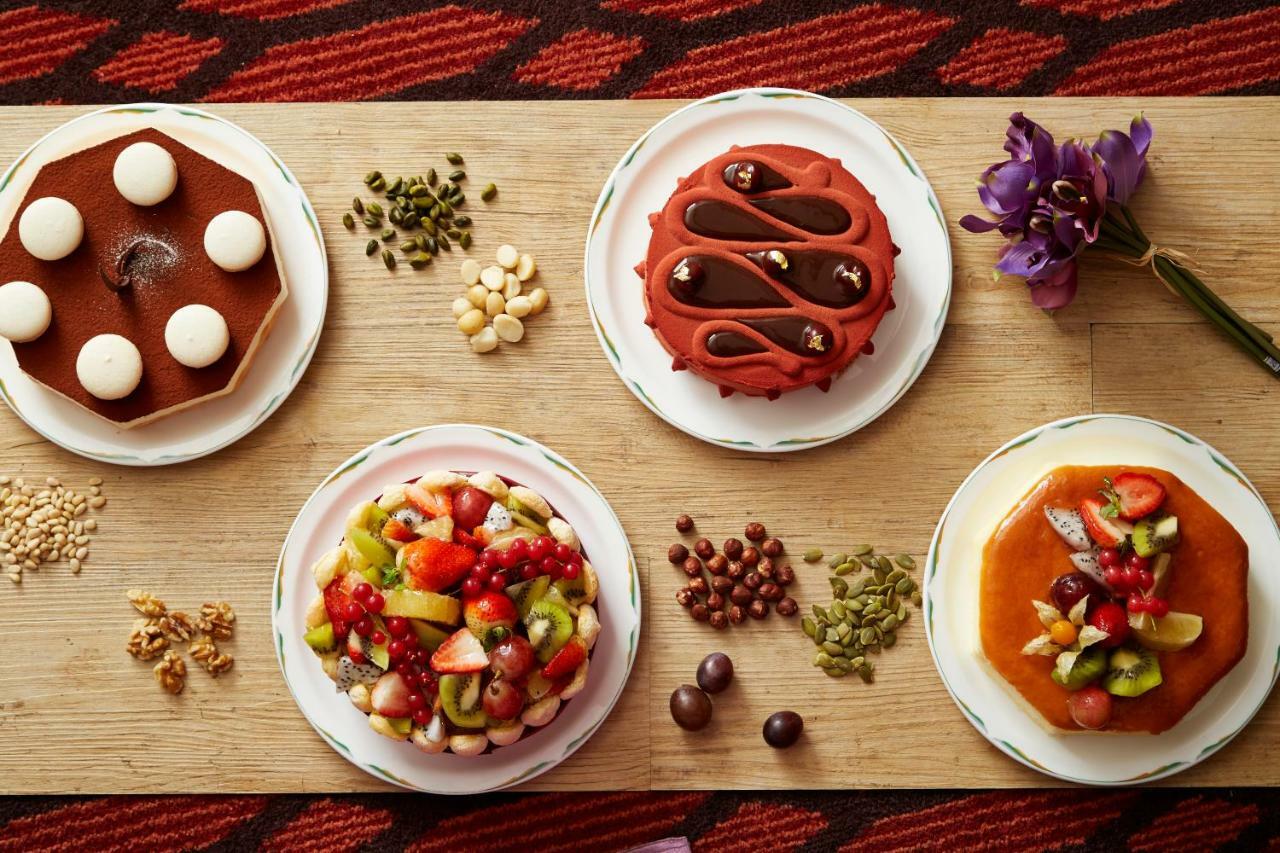 Evergreen Laurel Hotel - Taizhong Zewnętrze zdjęcie The photo displays a variety of desserts arranged on small plates. There are three main cakes or tarts:

1. **Top Left Plate**: A round chocolate cake with a smooth surface and white decorations on top.
2. **Top Middle Plate**: Another cake, possibly