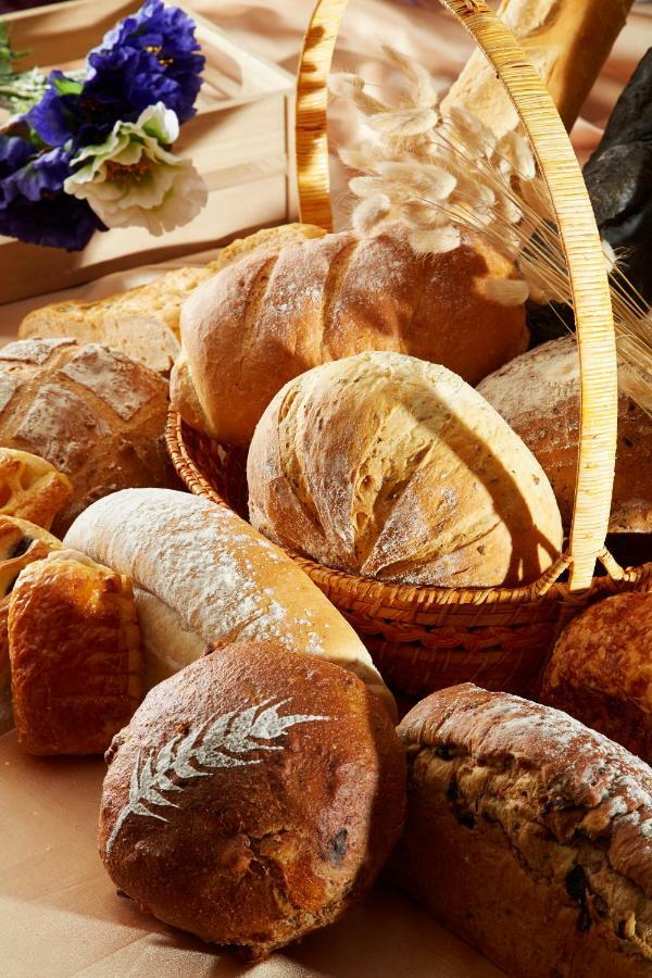 Evergreen Laurel Hotel - Taizhong Zewnętrze zdjęcie The photo shows a variety of freshly baked bread arranged in a woven basket. There are different types of bread, including round loaves, baguettes, and crusty rolls, showcasing a range of colors and textures. Some loaves have distinctive patterns or 