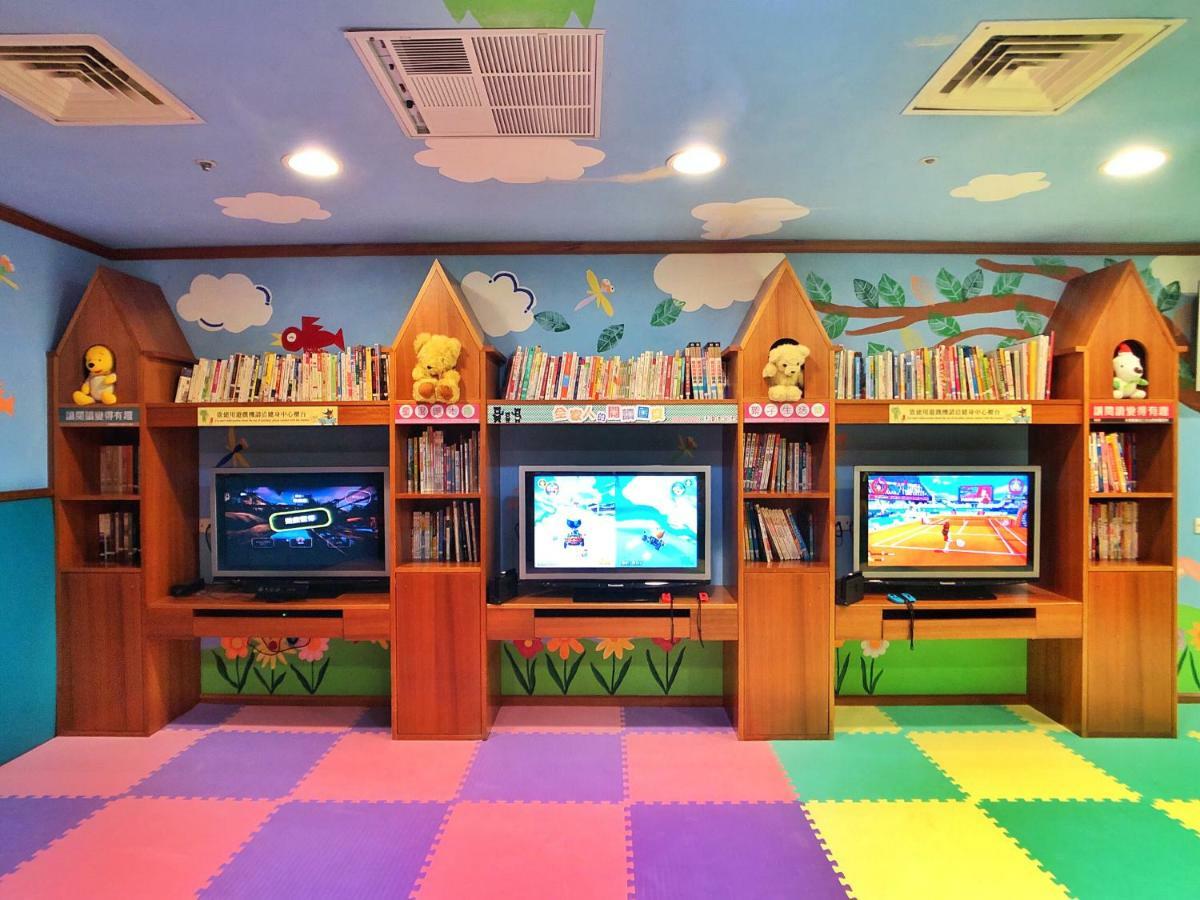 Evergreen Laurel Hotel - Taizhong Zewnętrze zdjęcie The photo shows a colorful and playful room designed for children. In the center, there are three wooden gaming stations, each equipped with a television screen and surrounded by shelves filled with books. The walls are decorated with cheerful images