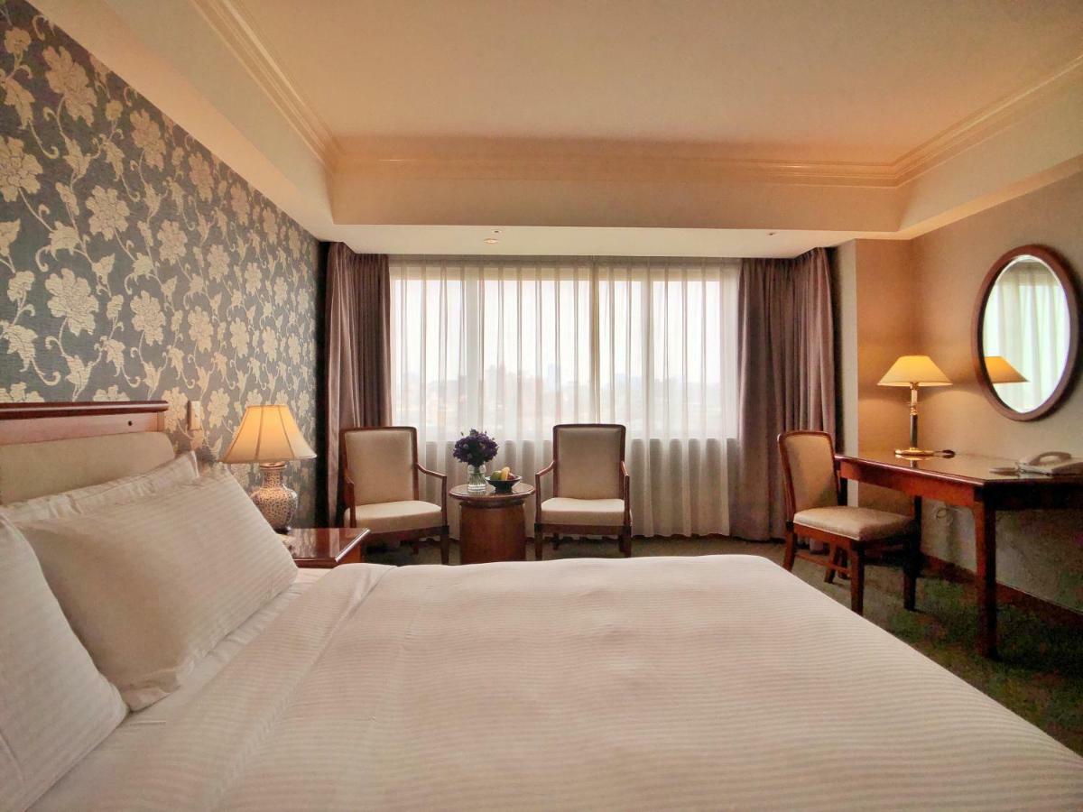 Evergreen Laurel Hotel - Taizhong Zewnętrze zdjęcie The photo shows a hotel room with a comfortable and inviting design. There is a large bed with crisp white bedding on the left side of the image. To the right, there are two elegant chairs with a small round table between them, adorned with a bouquet
