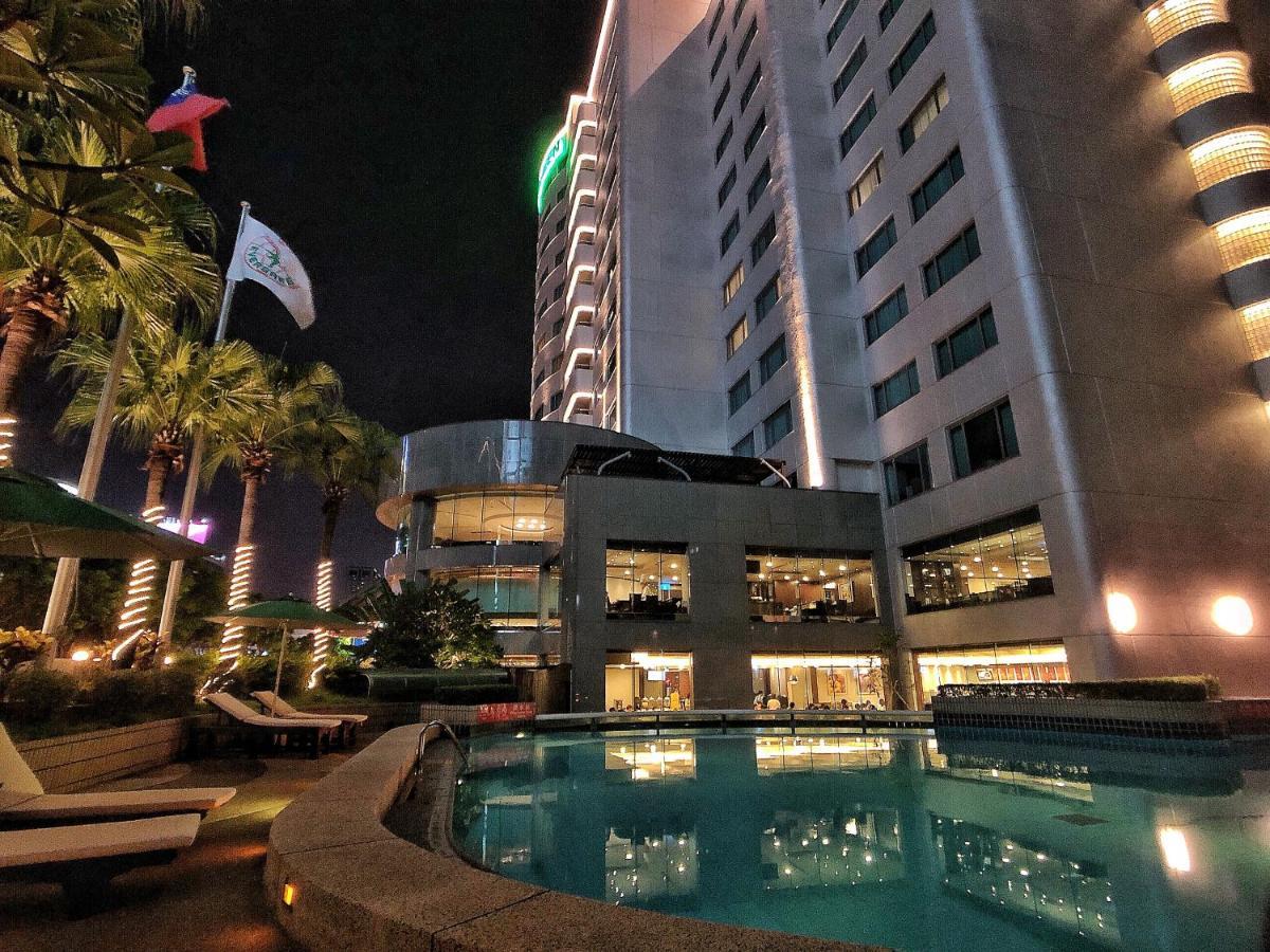 Evergreen Laurel Hotel - Taizhong Zewnętrze zdjęcie The photo depicts a modern hotel or building at night, featuring a sleek facade illuminated by lights. In the foreground, there is a swimming pool that reflects the surrounding lights and palm trees. There are lounge chairs near the pool, and the atm